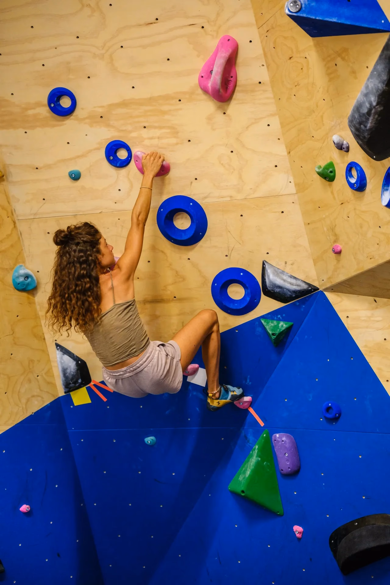 Climber in verticale su parete blu e legno con prese rosa